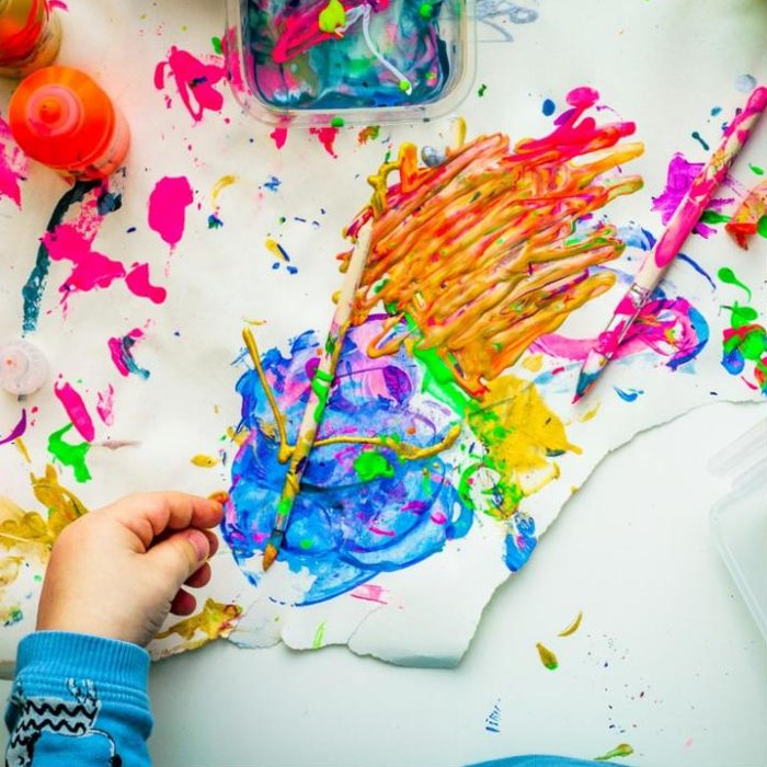 Child's hand next to a colourful painting with brushes