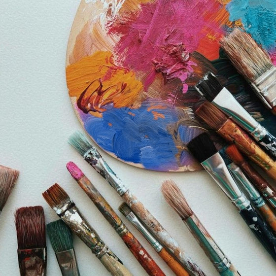 Paint palette with pink, orange and blue next to brushes